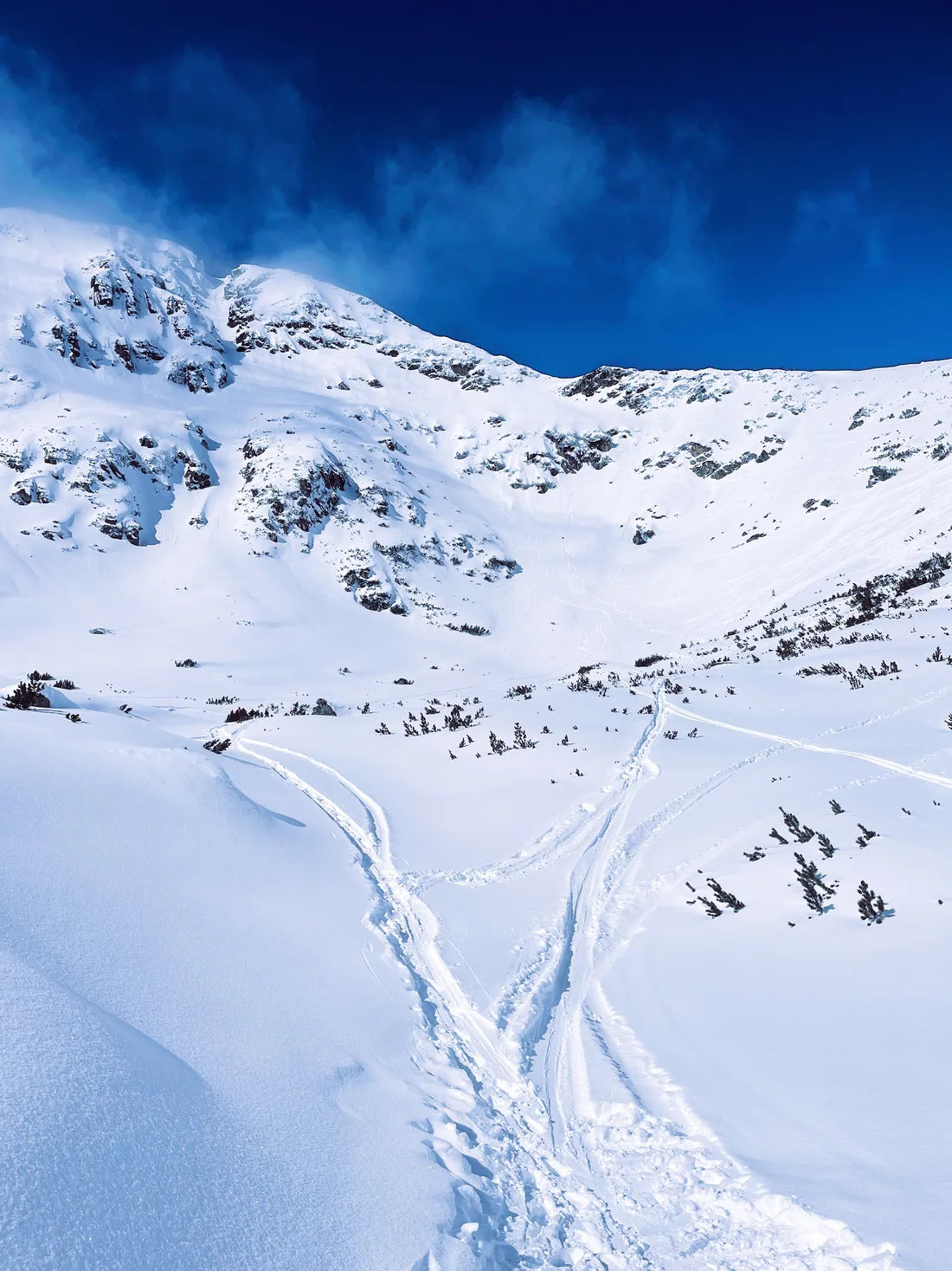 Snowy Bansko mountain under a deep blue sky, with tracks in the foreground