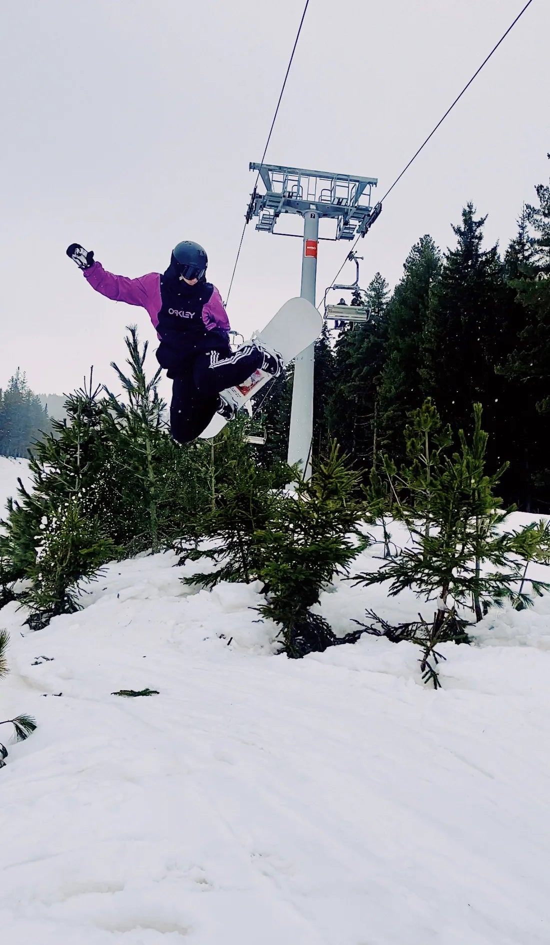A snowboarder jumping beside snowy trees and a chairlift in Bansko